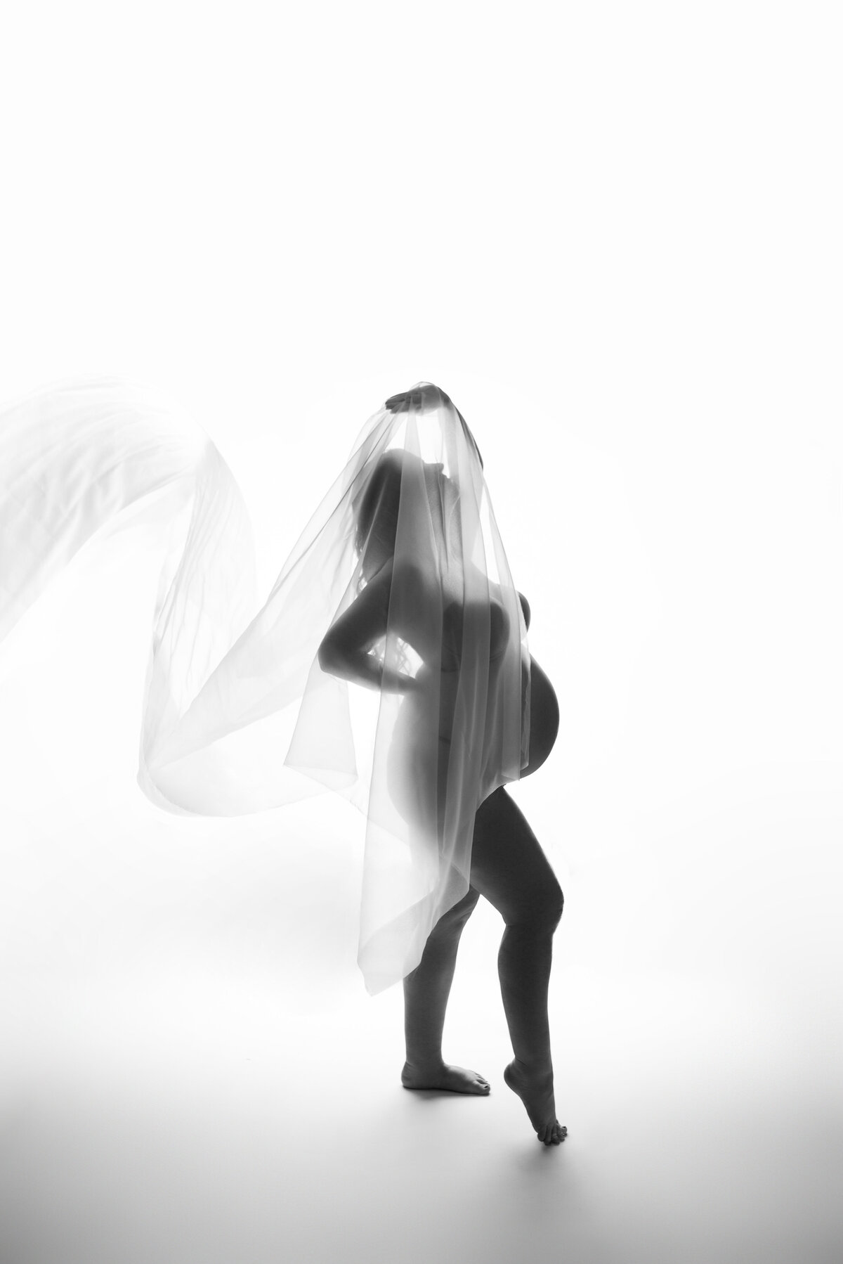 Maternity photo shoot with Maternity and Newborn Studio of Atlanta by Casey McMinn Photography of pregnant woman posing nude with sheer fabric in a black and white silhouette shot.