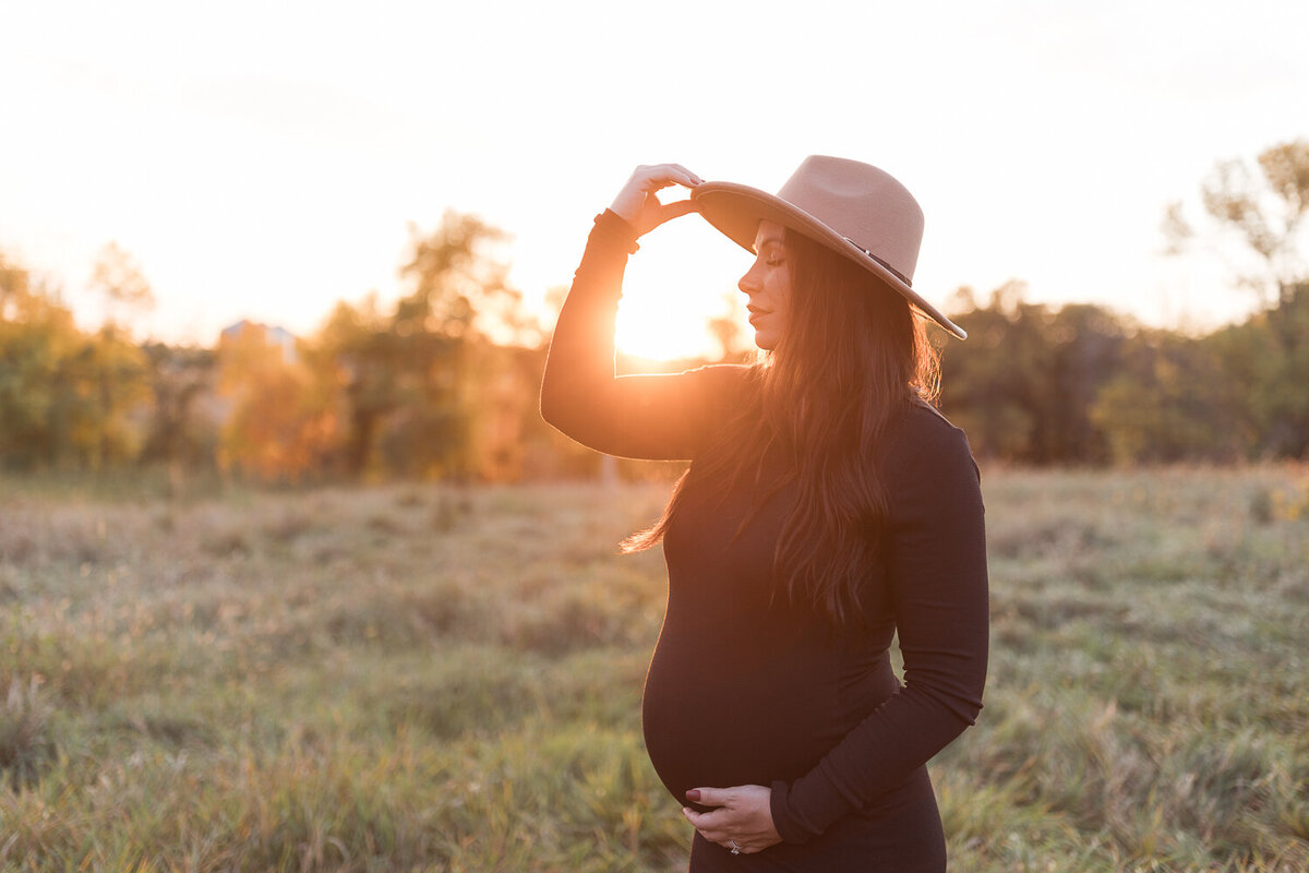 pregnant mom holding brim of hat outside