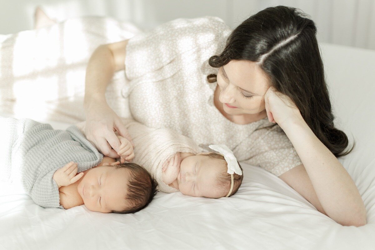 mom caresses newborn twins on studio bed in houston