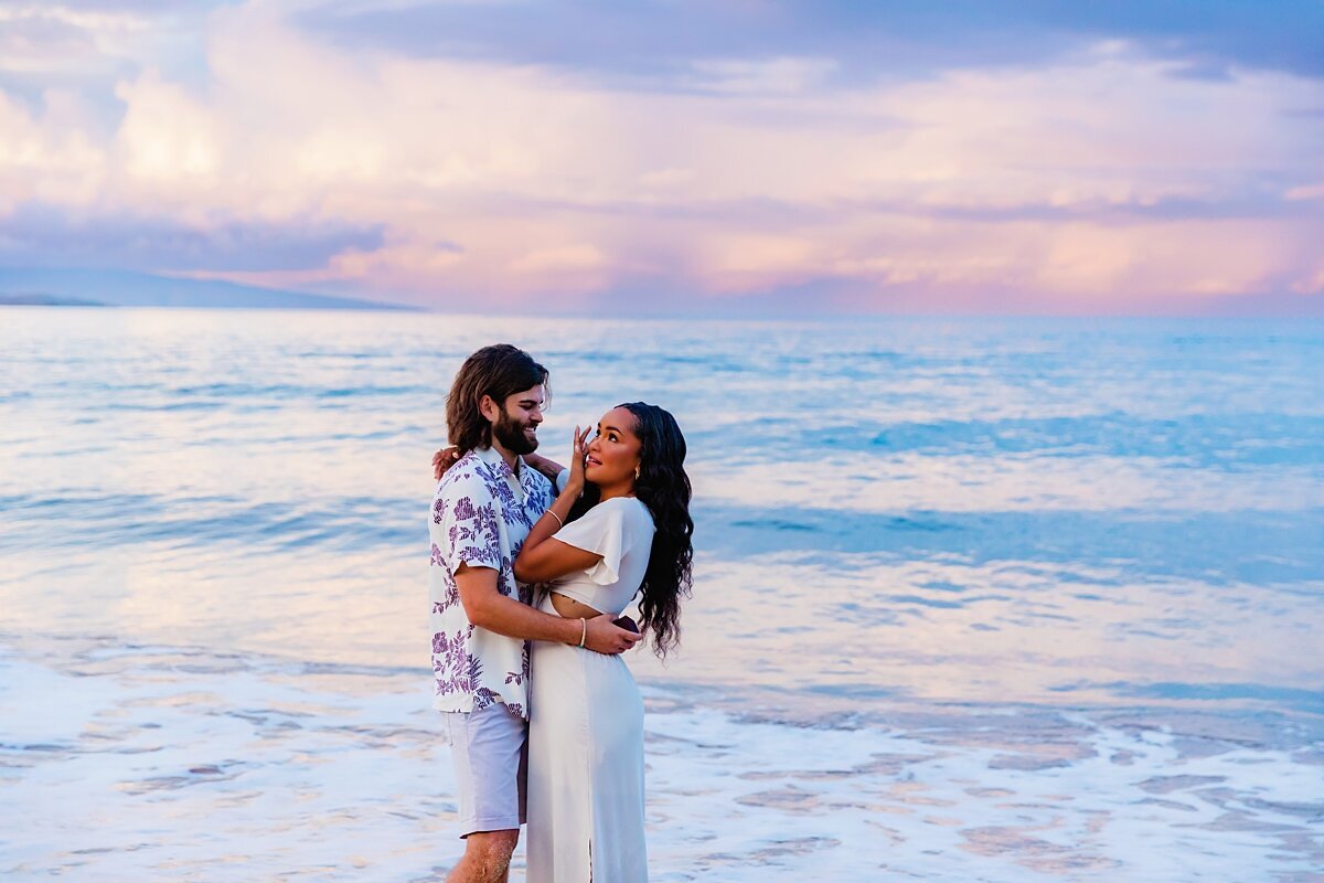 Man embraces his new fiance in front of their engagement photographer in Maui on the beach