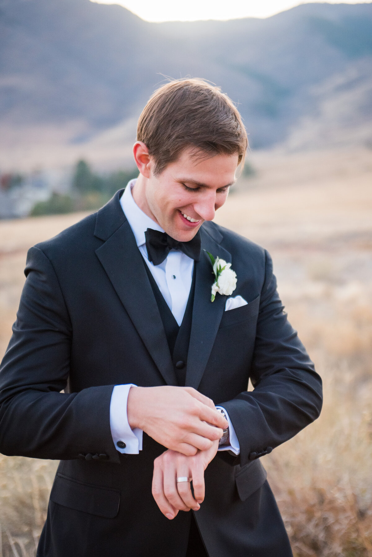 A groom smiles and glances down at his watch at The Manor House in Colorado.