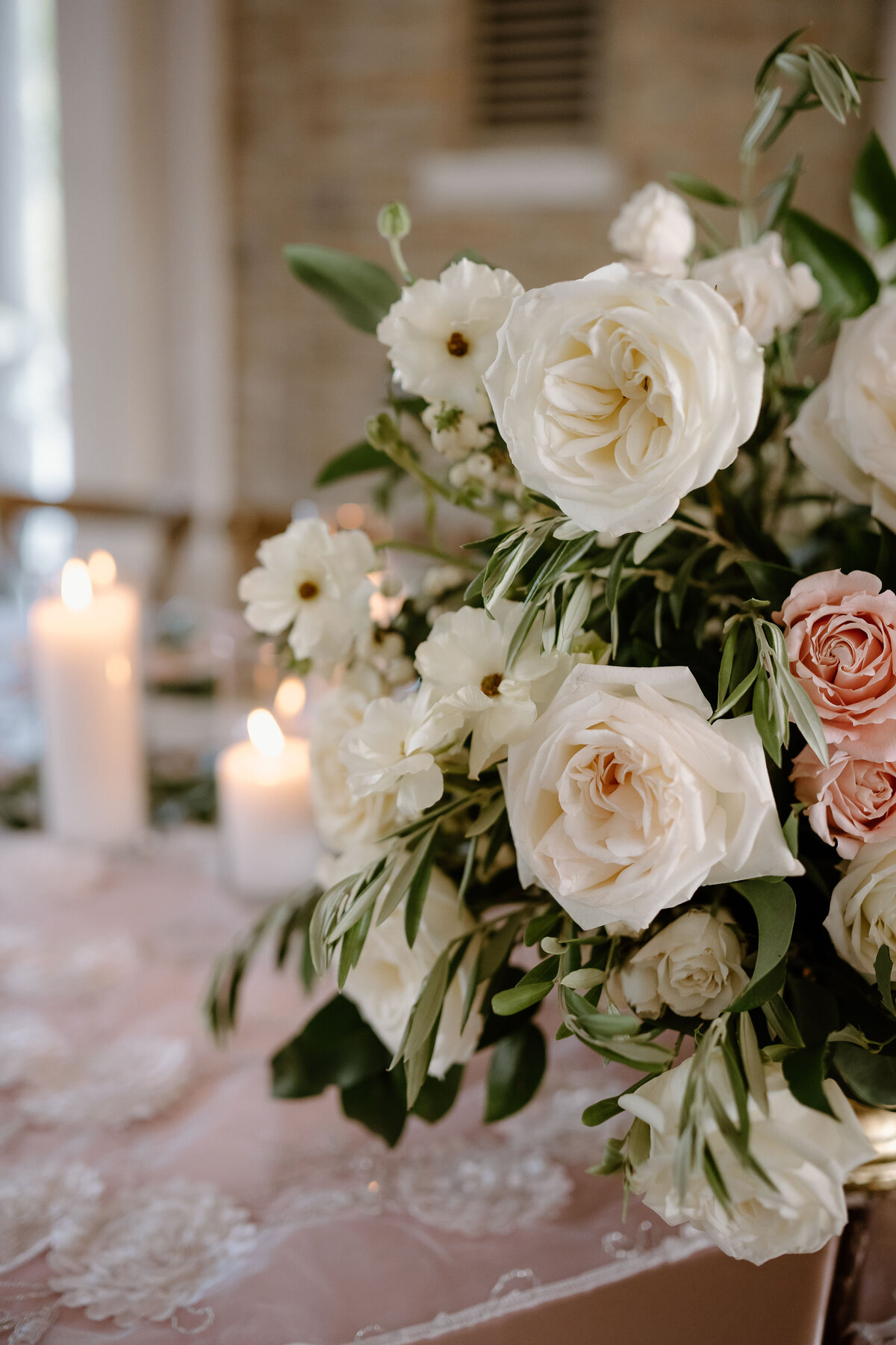 Romantic wedding centerpiece with ivory roses, blush blooms, greenery, and glowing candlelight.