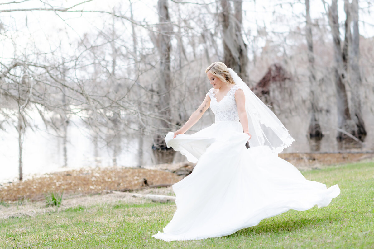 outdoor weddin gphoto of bride dancing on green grass next to a lake as her dress flows beneath her