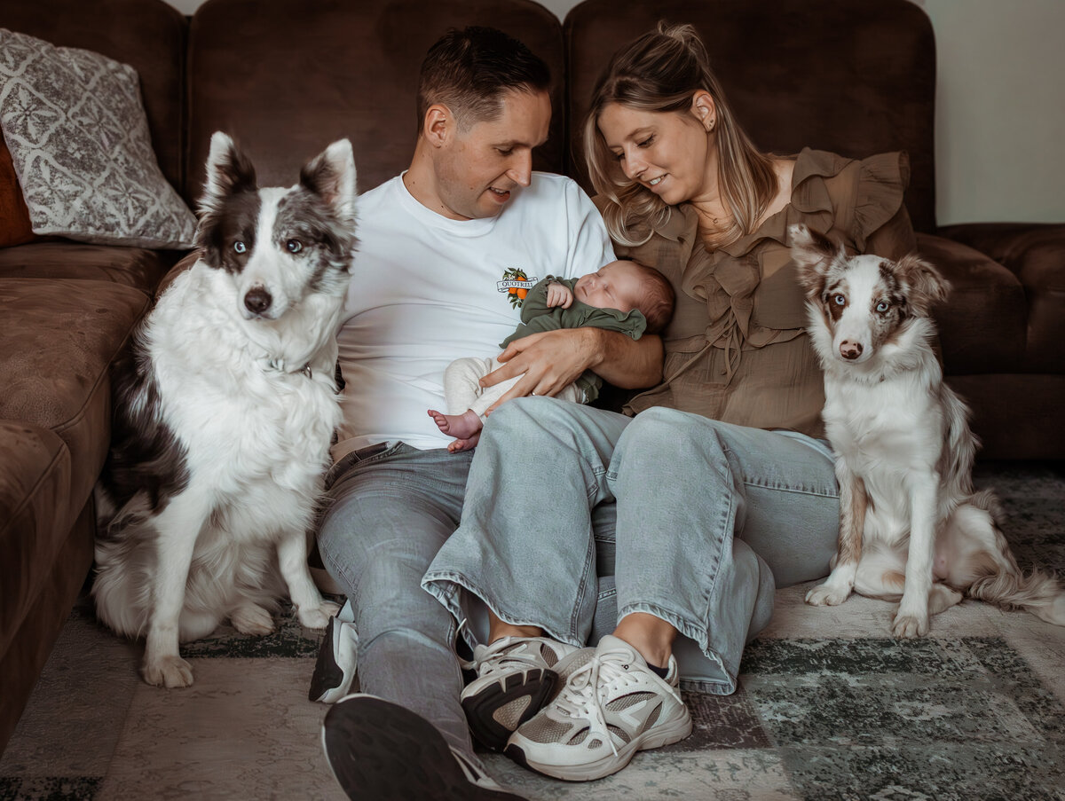 gezin zit voor de bank met baby en twee honden en kijken naar de baby
