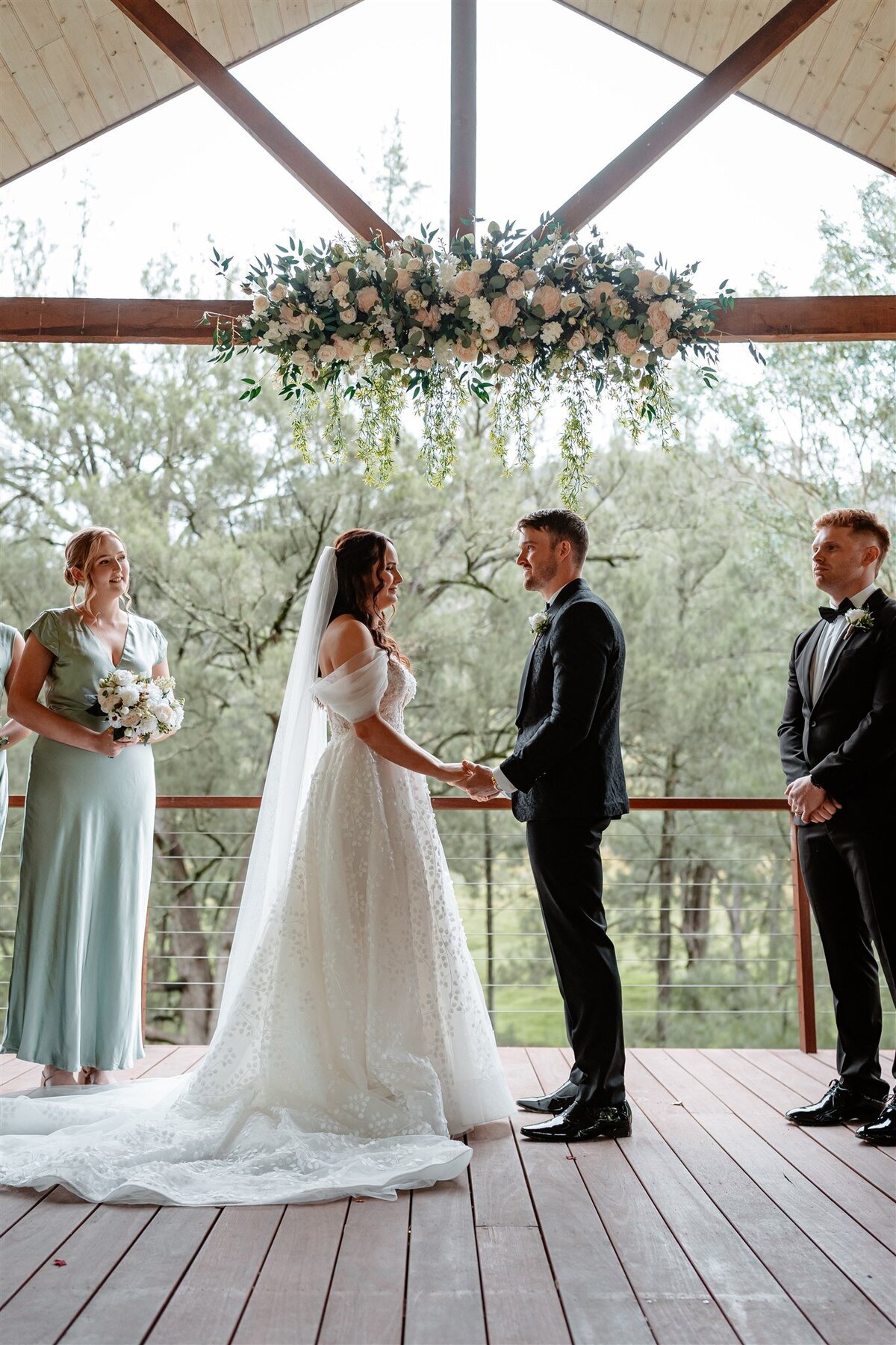The bride, radiant in her flowing white gown, exchanges heartfelt vows with her groom under a canopy of blooming roses.