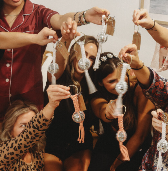Image showcasing unique, disco ball-themed favors or gifts held by members of The Bold Babe Society, highlighting the sense of community and shared experiences promoted on their website design.
