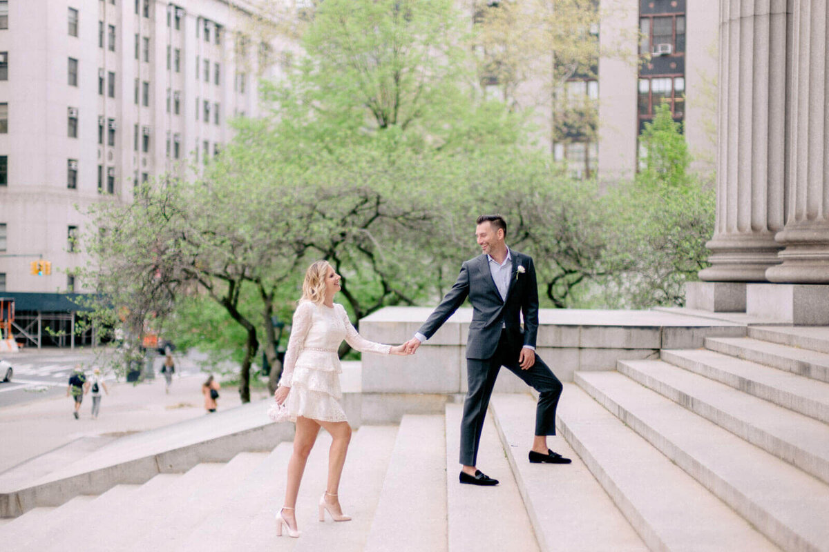 The eloping bride and groom are holding hands while climbing the grand staircase of the NY City Hall. Image by Jenny Fu Studio