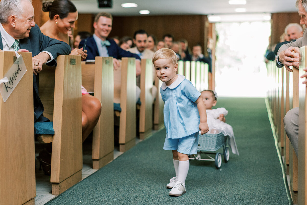 Ring bearer pulling a flower girl in a wagon down the aisle during a church ceremony in Cashiers North Carolina.