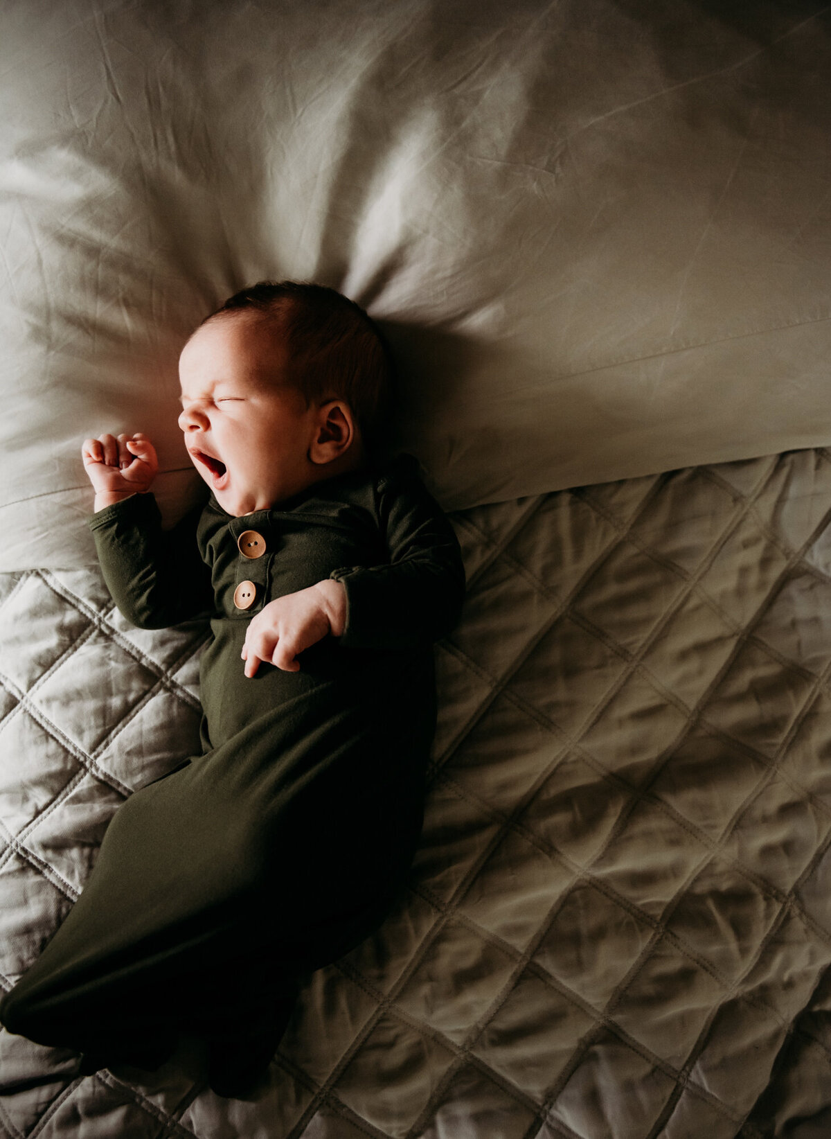 Newborn Photographer, Little boy in a green outfit yawning on a bed.