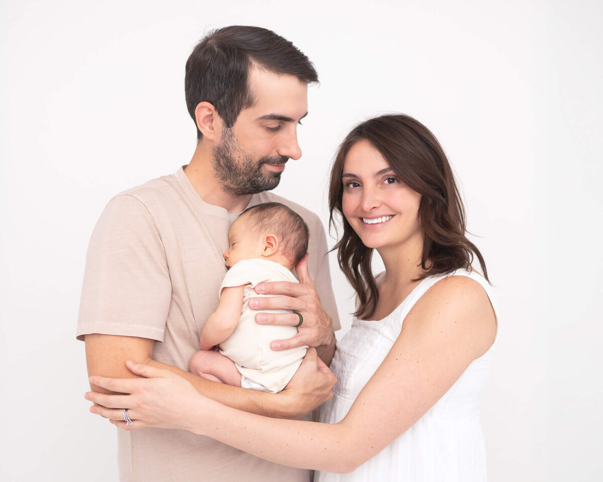 husband holding new baby embraced by new mom looking at her lovingly