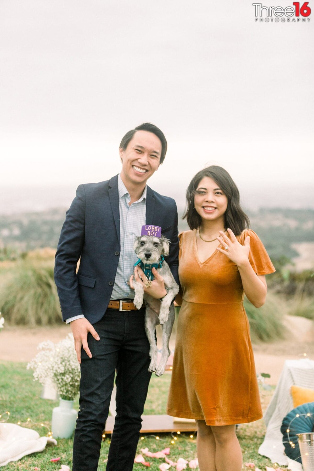 New Bride to be shows off her ring after accepting a marriage proposal while she poses with her fiance and dog