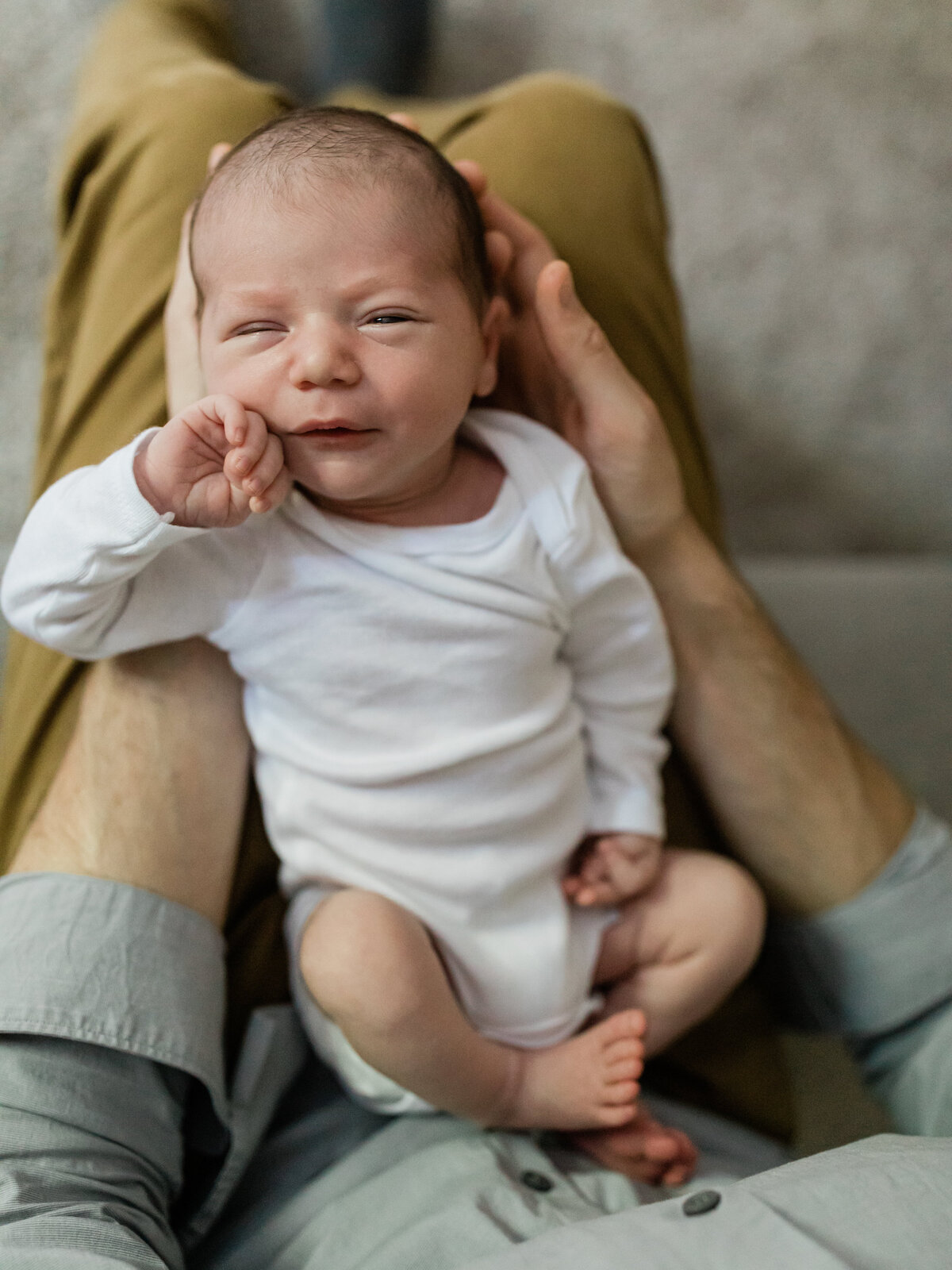 newborn baby boy laying in dads lap for in home lifestyle session