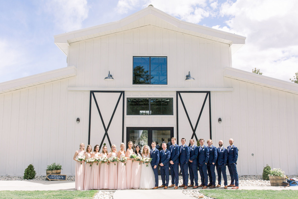 Bridal party standing in front of white barn at Woodlands Colorado wedding