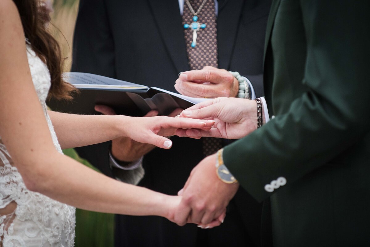 A close up shot of a groom placing the wedding band on his bride's finger.