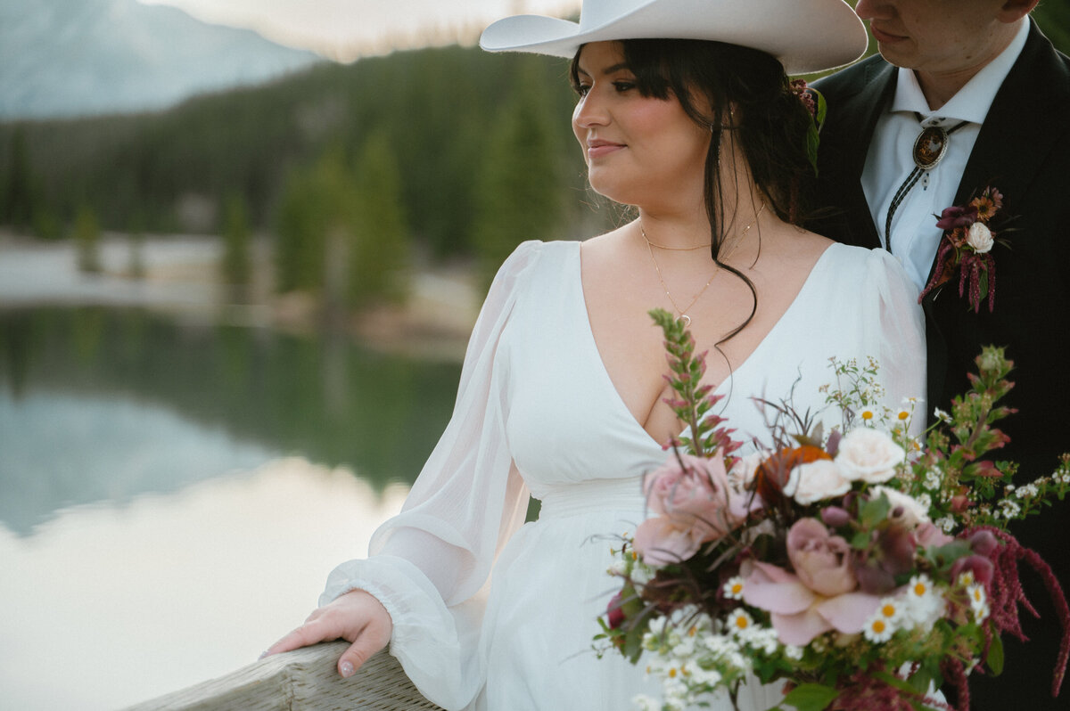 Cowgirl bride on wooden bridge with scenic river and forest in background.