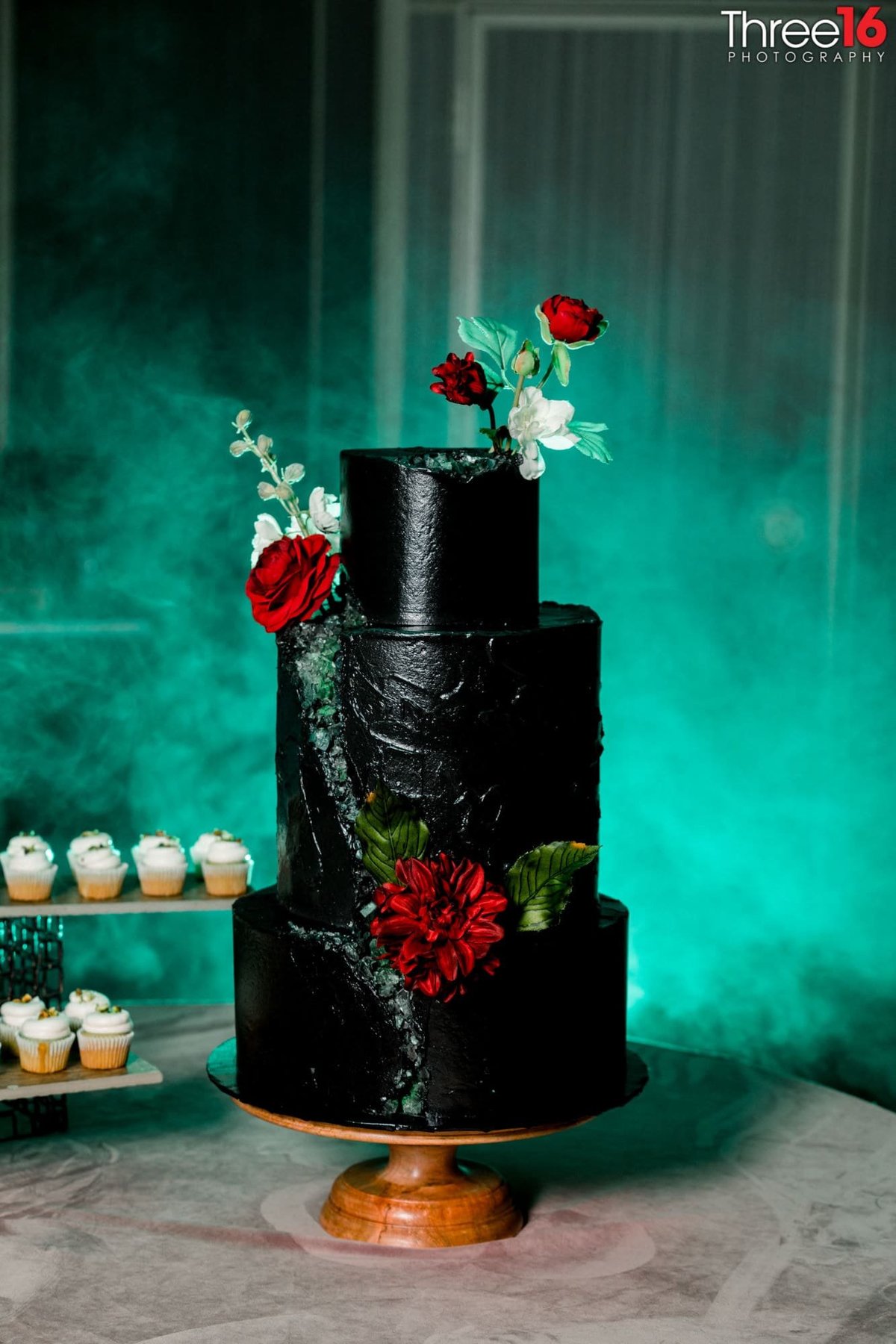 Three-tiered black wedding cake with red and white floral enhancements
