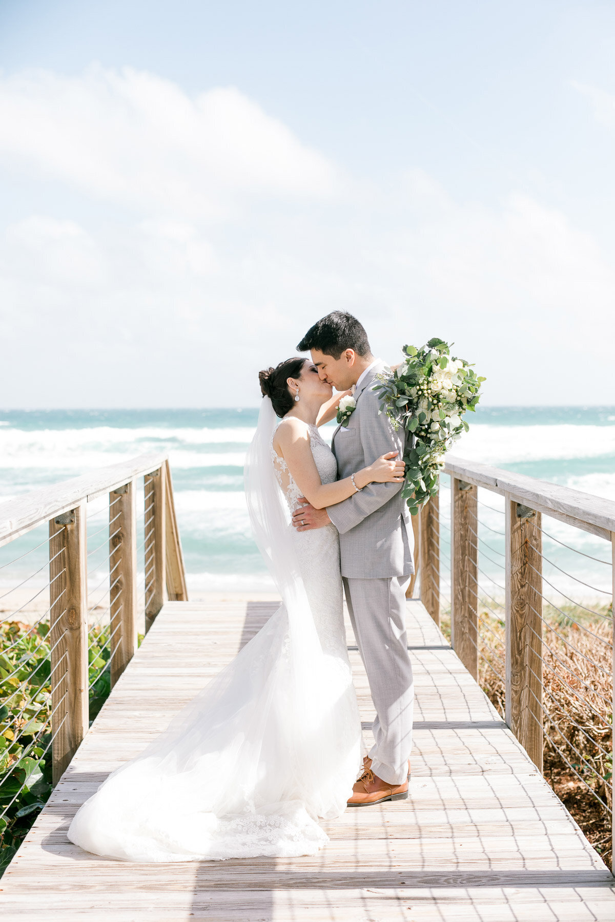 bride and groom kissing on beachwalk