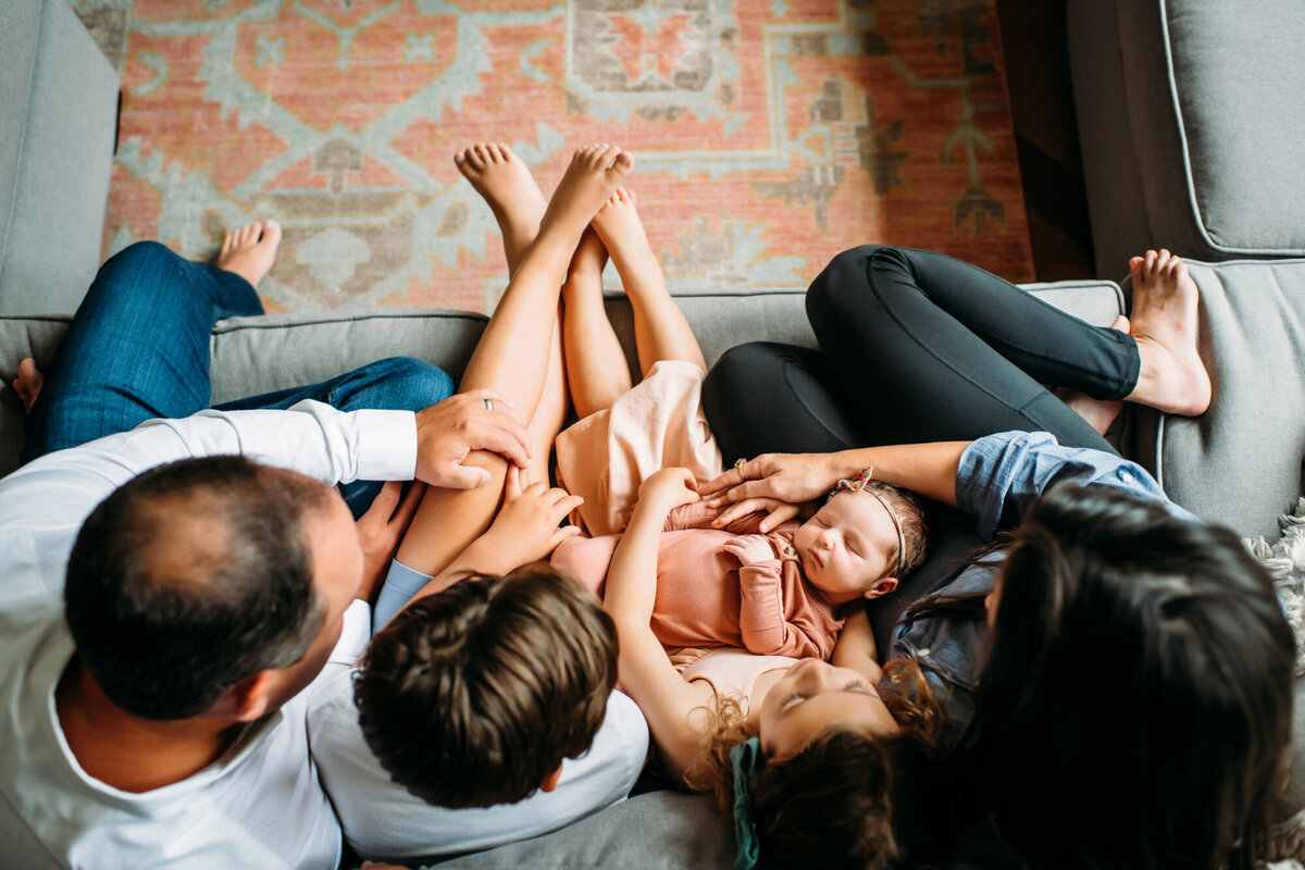 Newborn Photographer, Baby girl is on her family's lap on the couch.