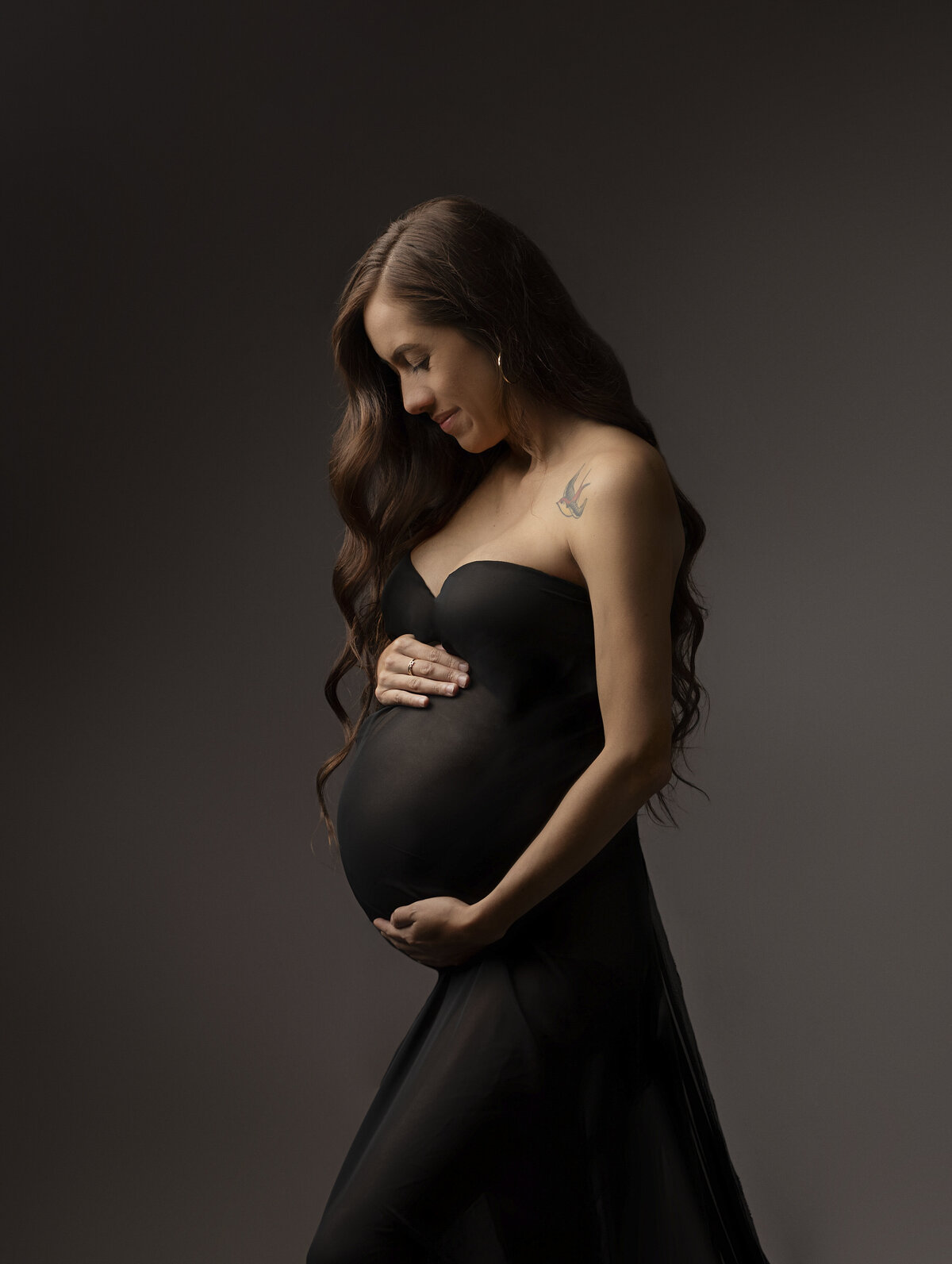 pregnant mother wrapped in black on brown backdrop looking down at stomach