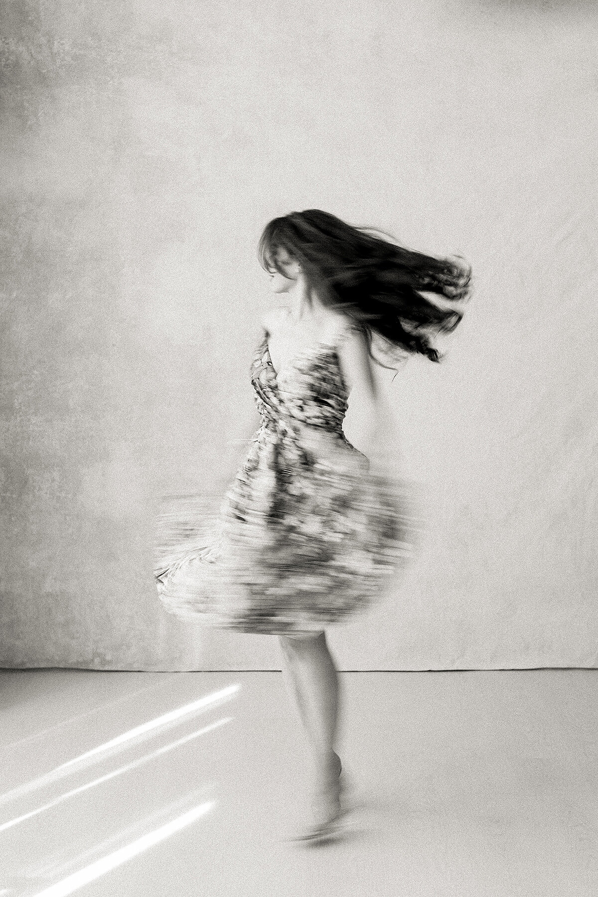 A beautiful black and white photo of a woman dancing in the middle of a Dallas photography studio for her boudoir session.