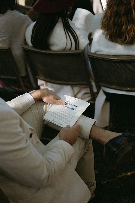 Zoom sur un livret de cérémonie posé sur les jambes d'un invité. Mariage au Château de beaussais en Bretagne.