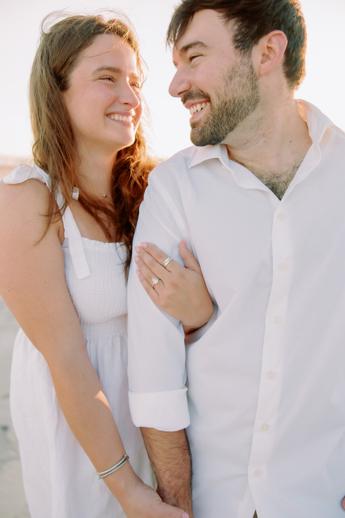 A close up of a person wrapping their arm around their partner's, showing off an engagement ring 
