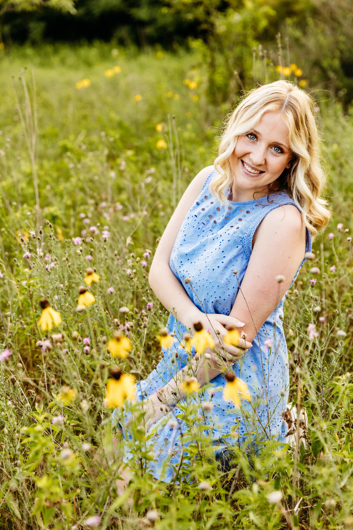 beautiful teenage girl with short blonde hair kneeling in wildflowers for her senior photos