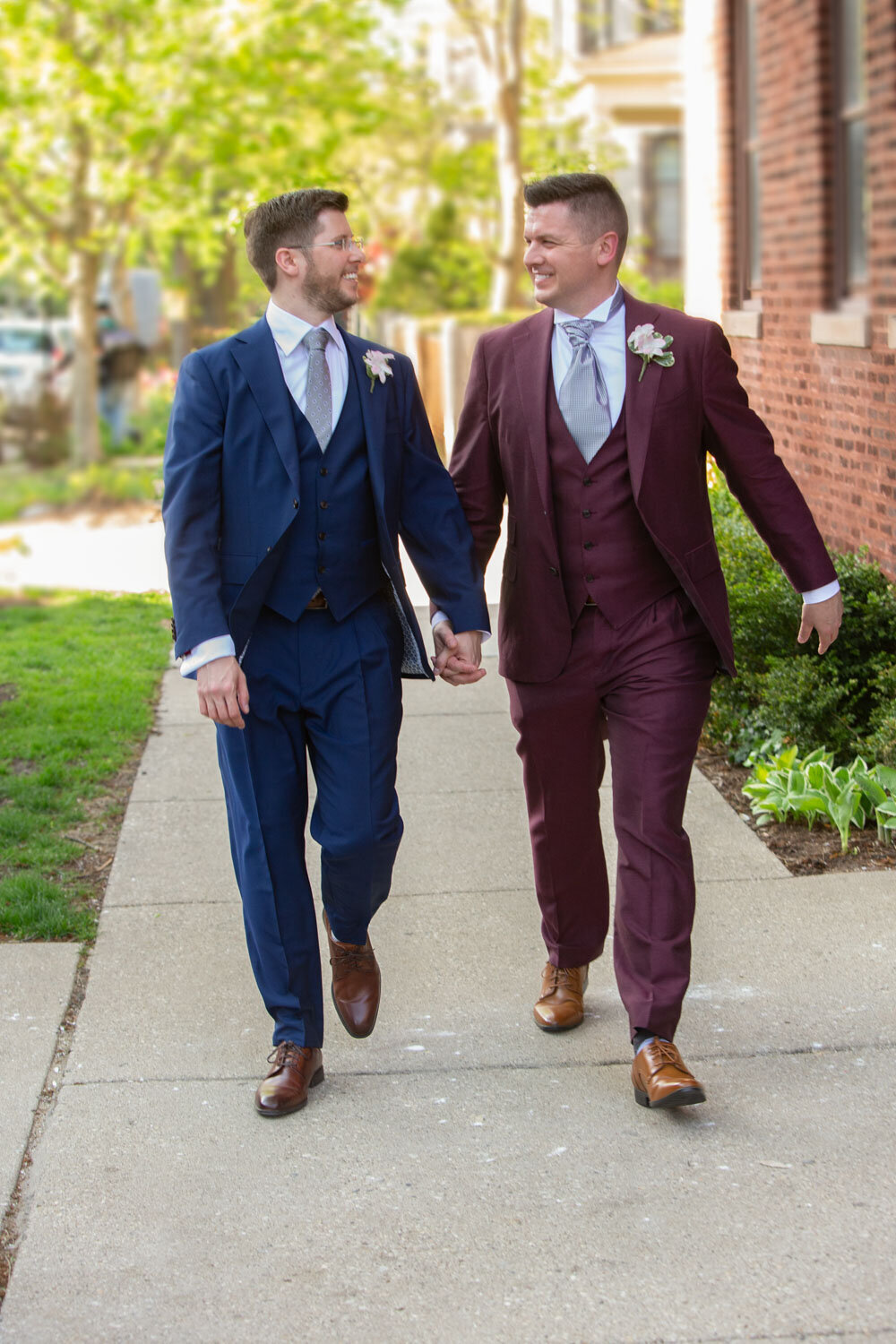 Two men in suits are walking down a sidewalk holding hands