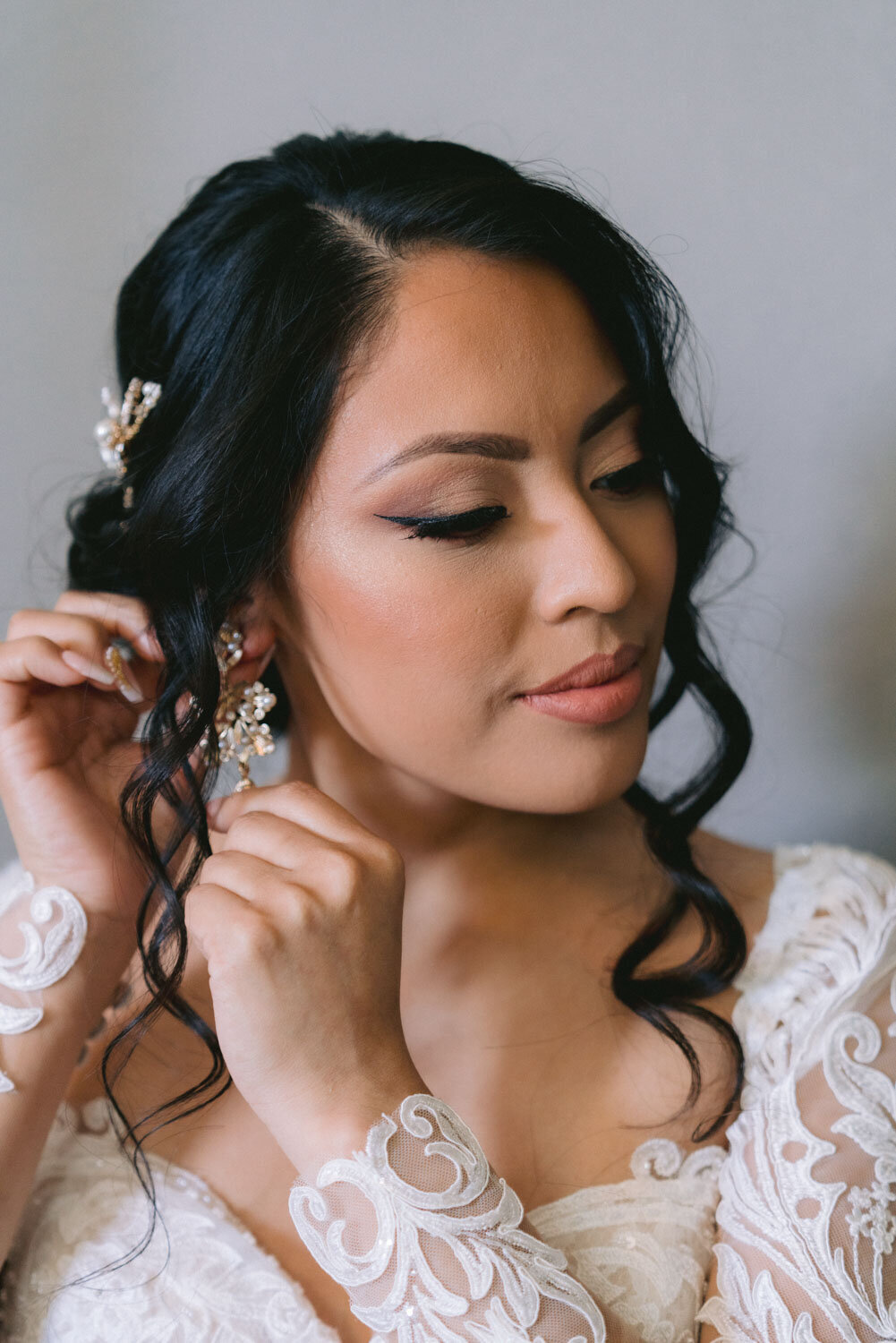 Bride adjusting her earrings, with her hair styled in loose curls
