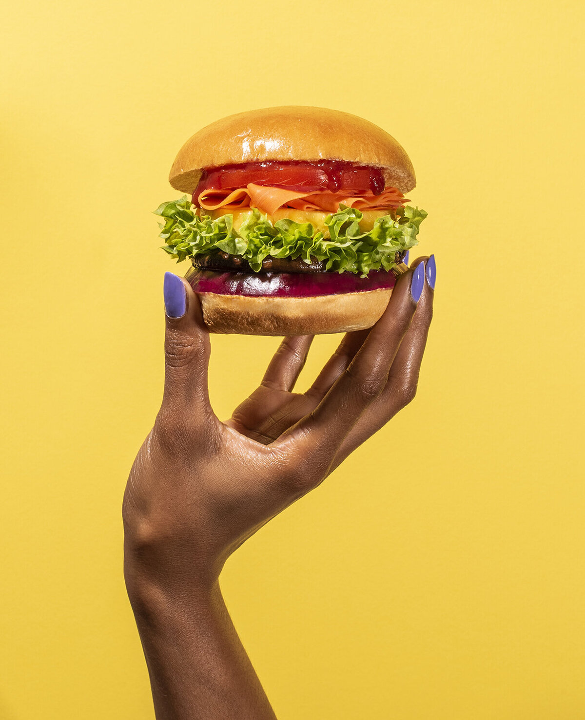 rainbow veggie burger hand model against yellow