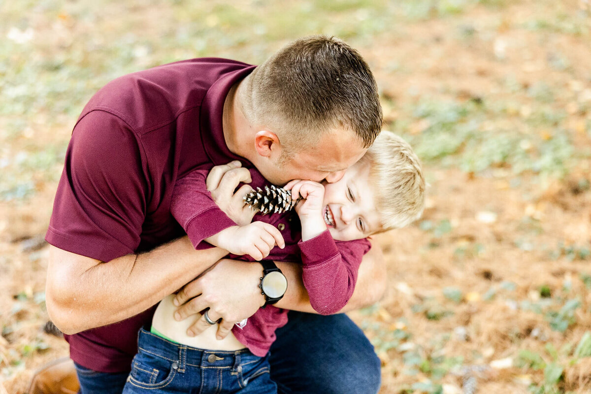 Father hugging son holding s pine cone during a fall family  photography session near Naperville, IL.
