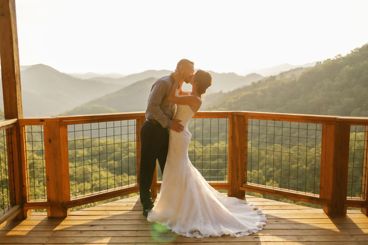 airbnb cabin wedding with bride holding her grooms face and kissing him passionately on a balcony with the Smoky Mountains in the distance