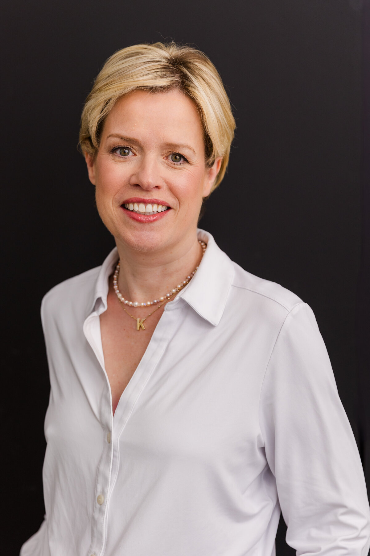 woman with short blonde hair standing in front of black background wearing corporate outfit white shirt during headshot photoshoot with Laure Photography