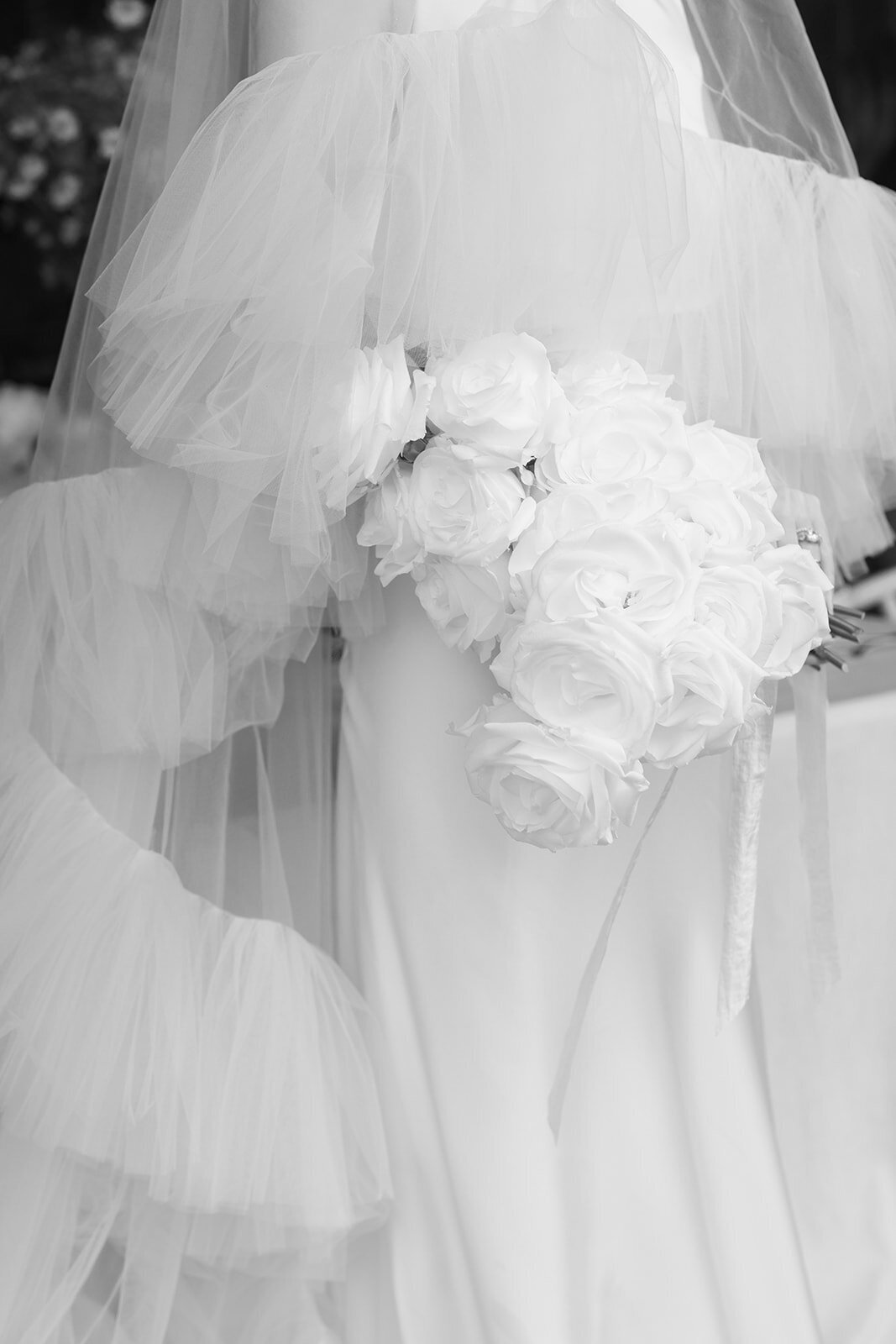 Black and white photo of a bride's ruffled veil and white bouquet
