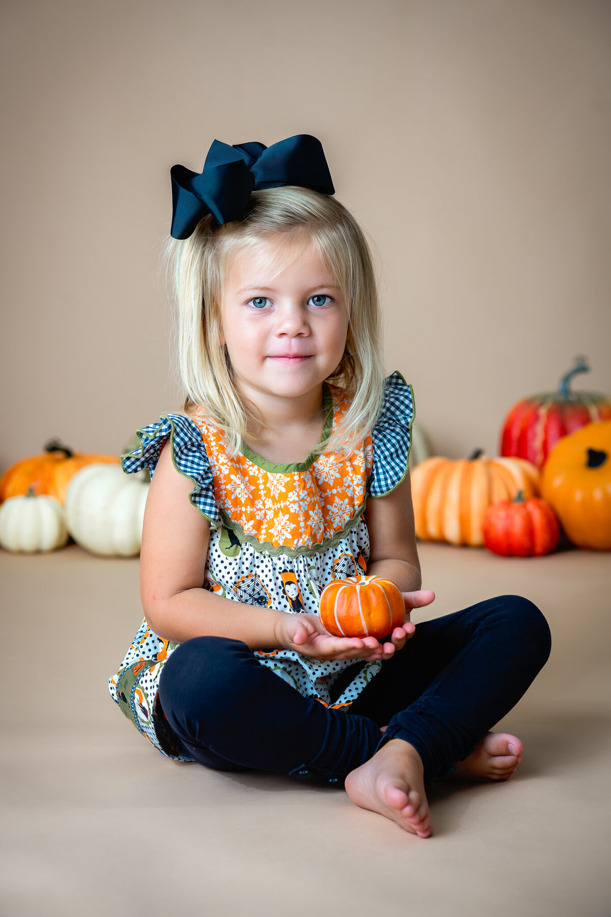 A young girl is holding a pumpkin while she poses for a Halloween photo session.