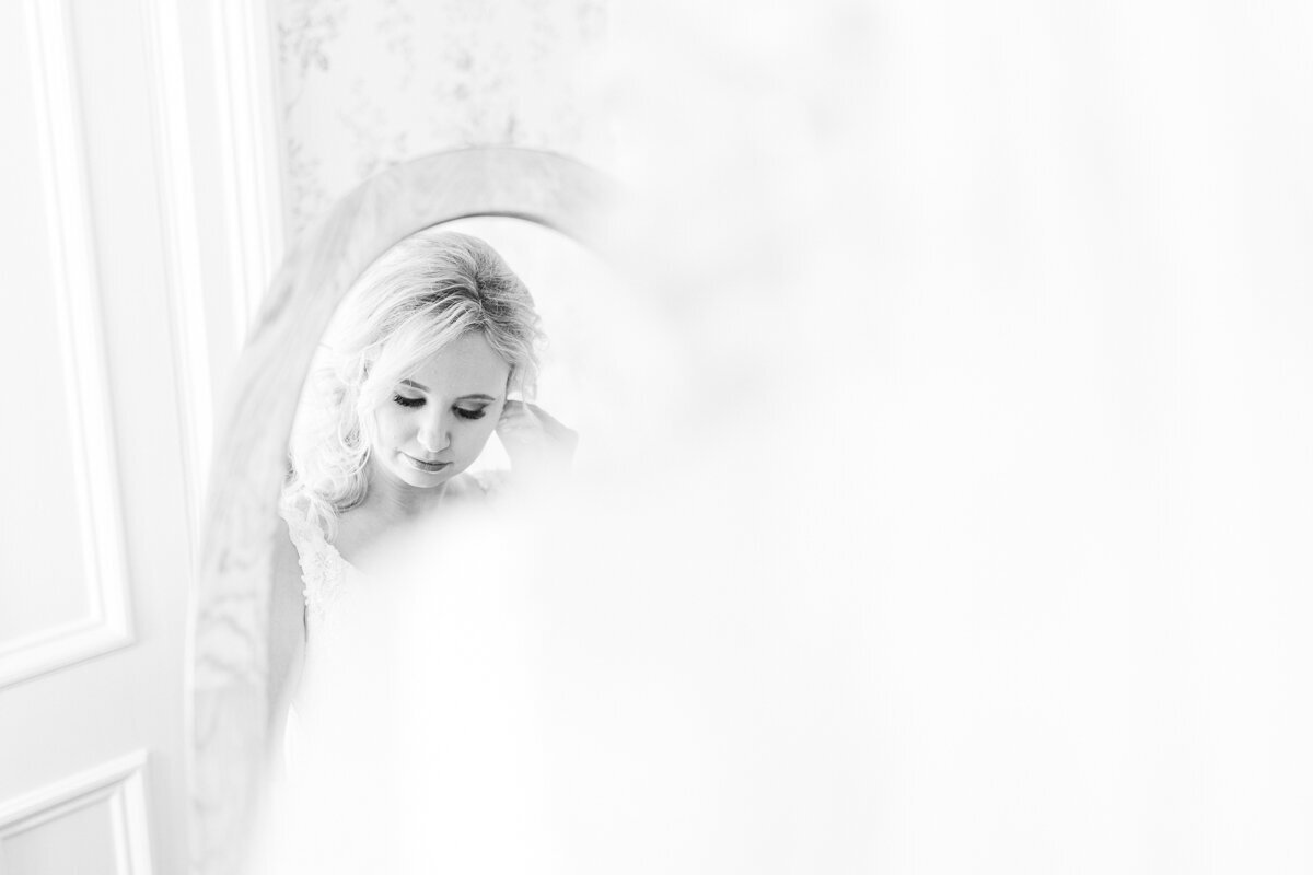 Black and white image of bride putting on her earrings in the mirror in Ithaca, NY