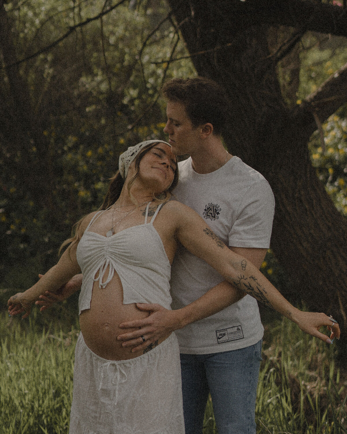 Mom-to-be with husband holding belly during outdoor storytelling maternity session.