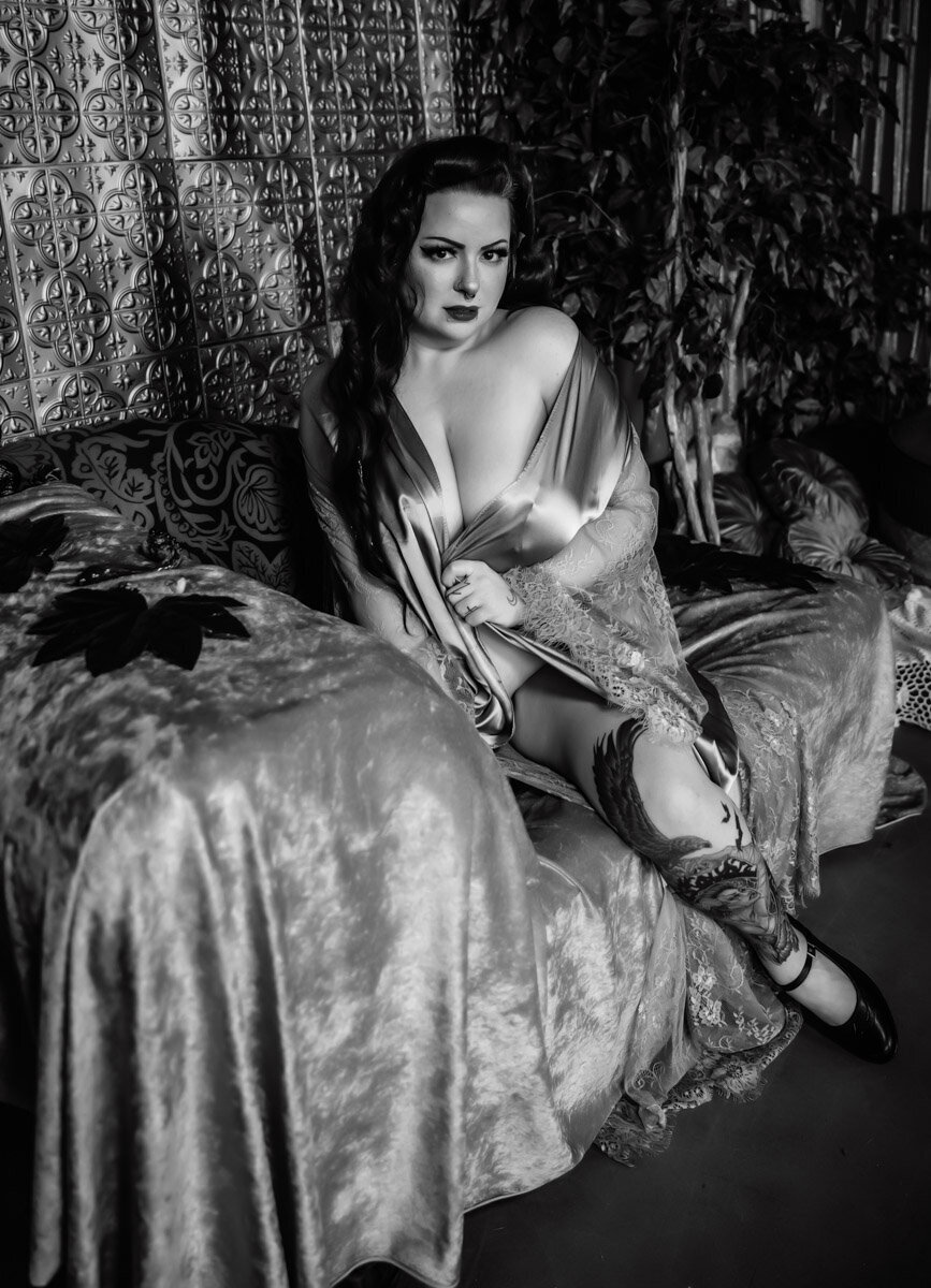 black and white photo of a woman sitting on a chaise in a vintage robe and pinup hair