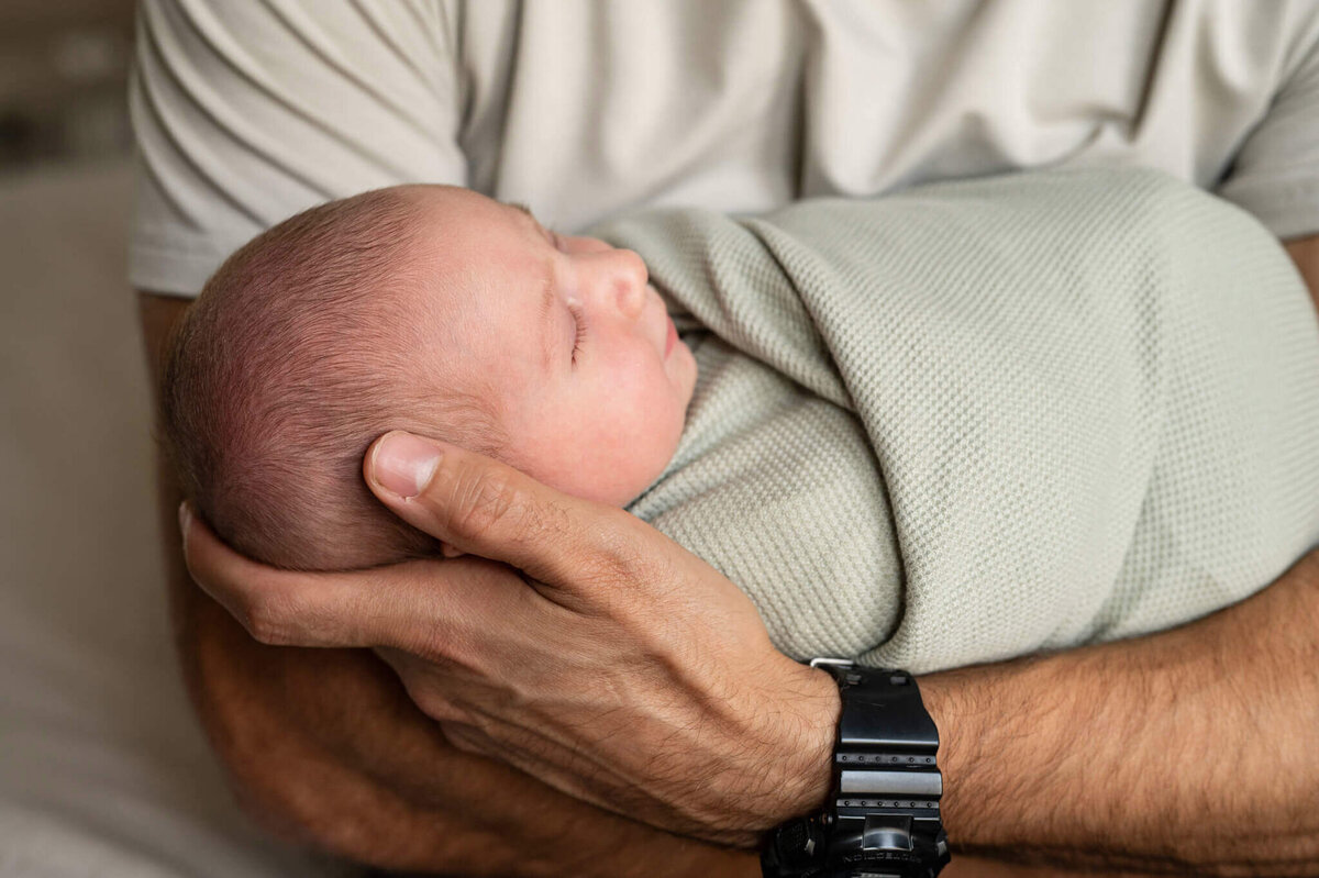 Up close shot of newborn baby in green swaddle while dad holds him