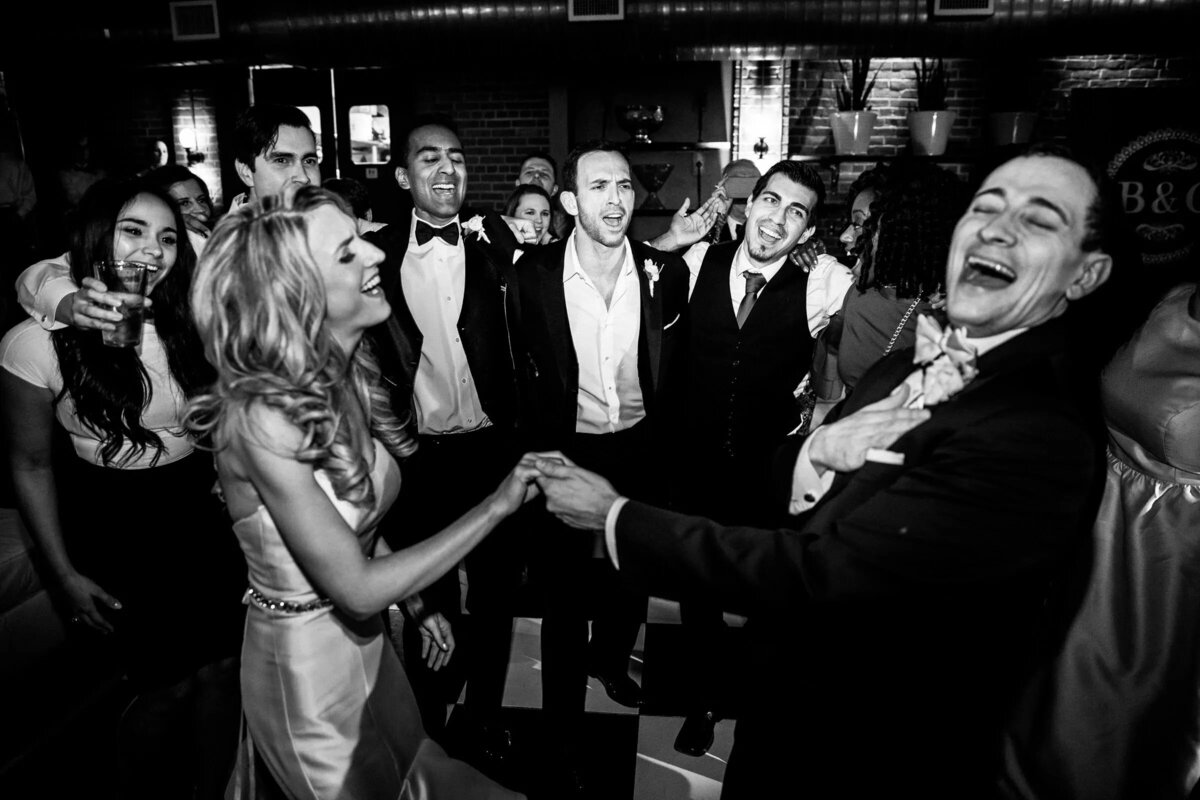 Euphoric moment as a bride dances surrounded by wedding guests, with laughter and celebration captured in black and white.