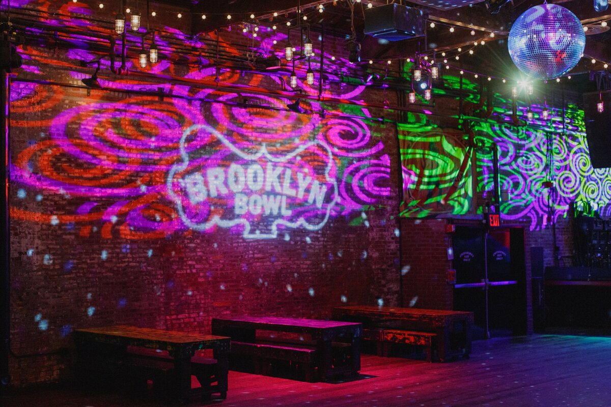 The Brooklyn Bowl logo projected in swirling neon lights across exposed brick walls.