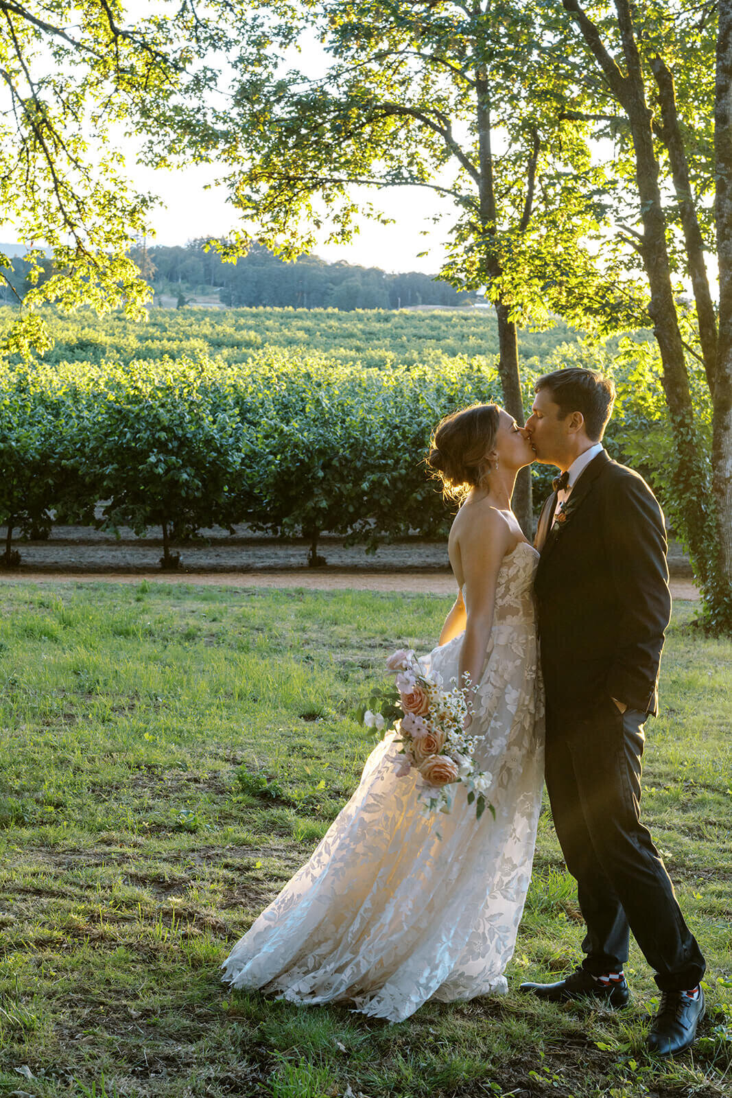 A bride and groom kiss with a vineyard in the backyard.