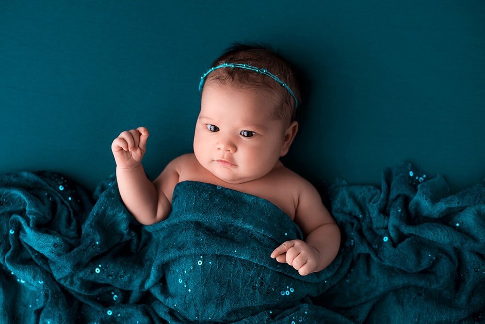 Baby girl with eyes open wrapped in sequin teal fabric at Downtown Vancouver newborn photoshoot