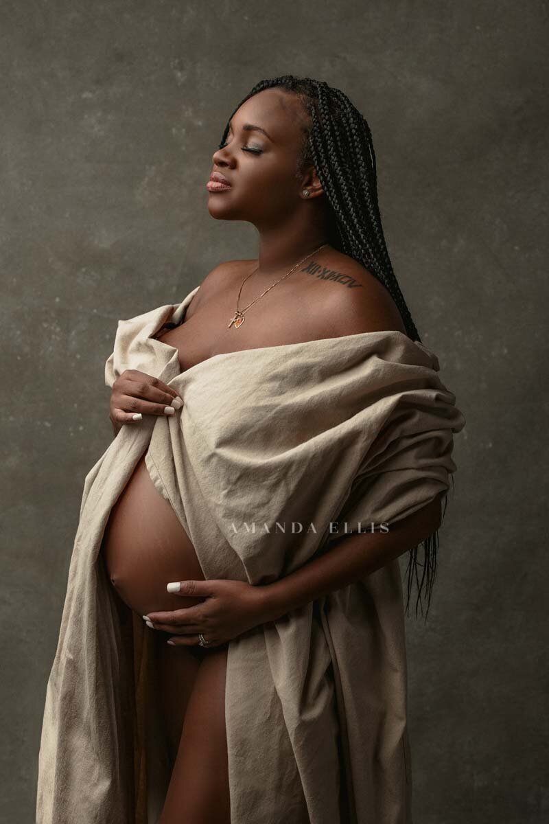 Maternity portrait of woman with braids posing with cream sheets