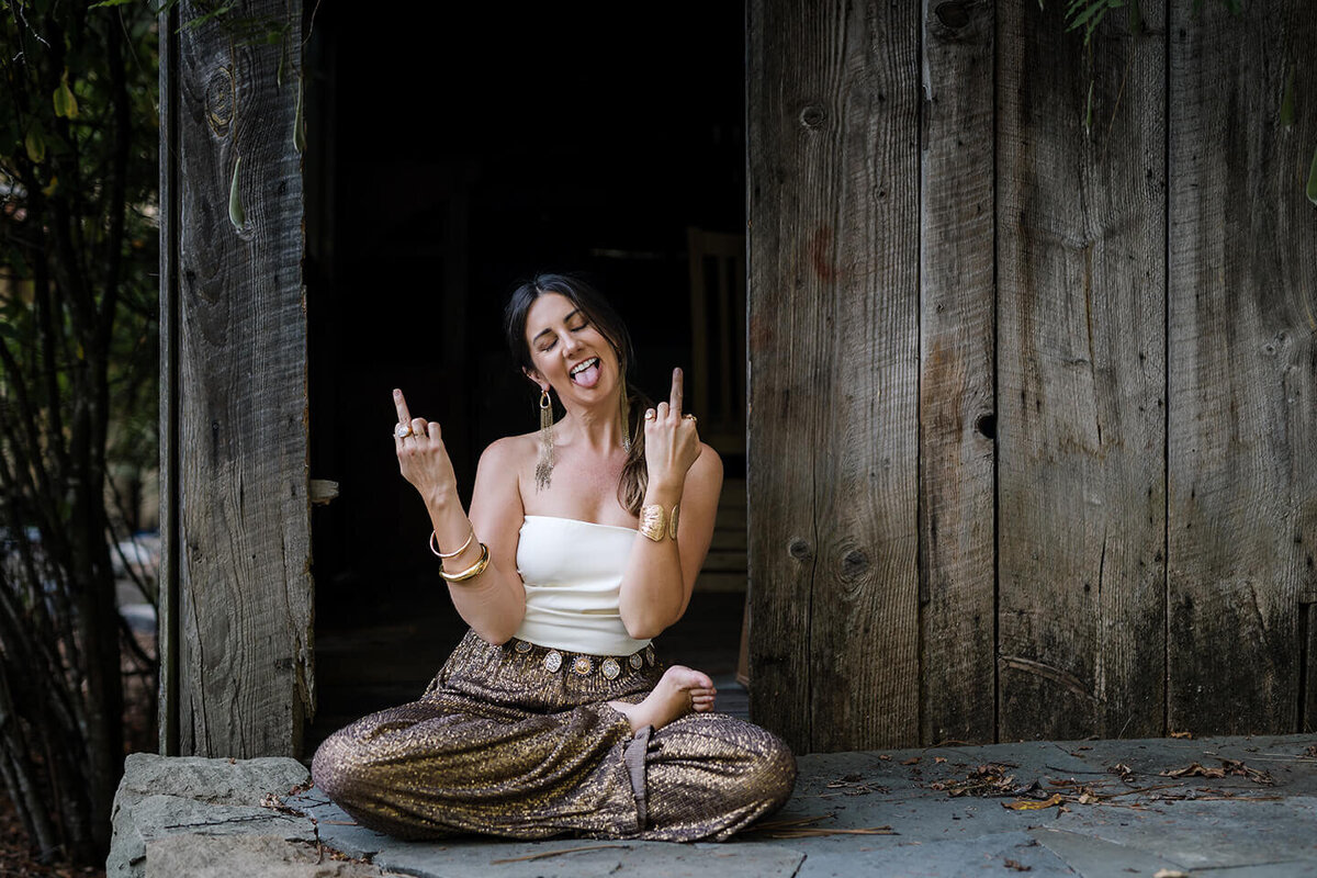 bold woman, sitting outside in rustic setting giving the finger with both hands to the camera