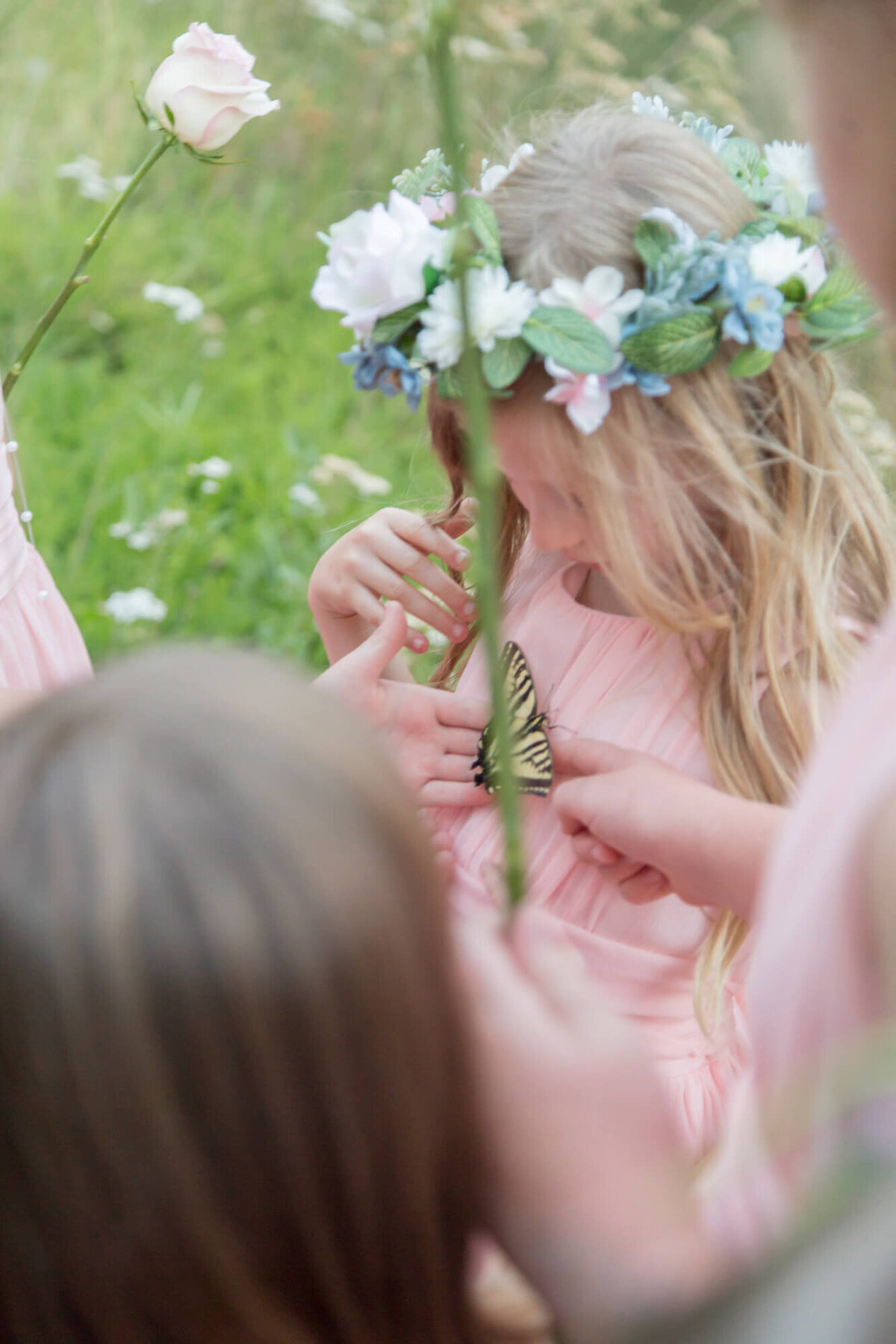 a little girl with a flower crown looking at a butterfly during a mountain wedding