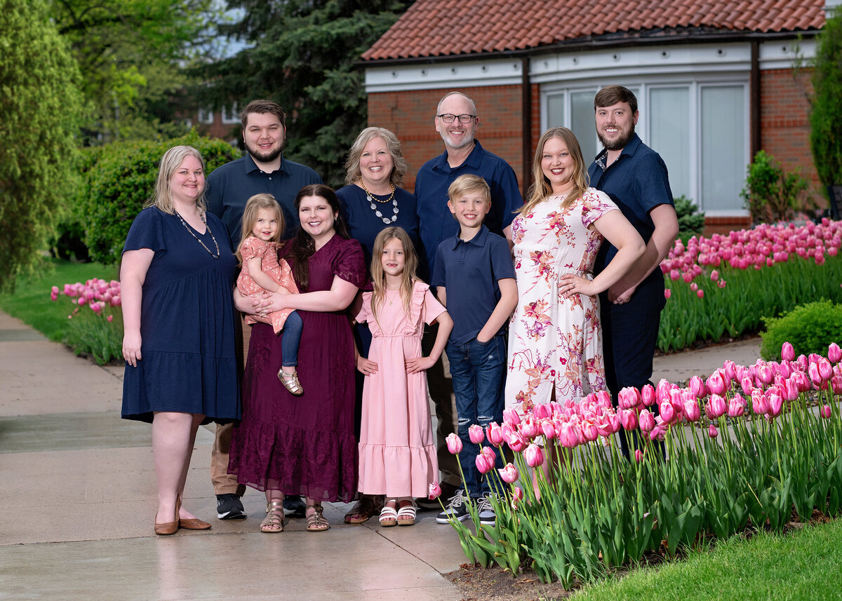 A cheerful extended family poses among blooming tulips on a spring day, with smiles and coordinated outfits in a garden setting.