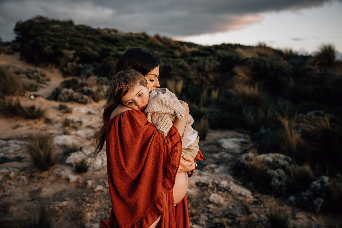 Pregnant mother cuddles son in beach maternity session