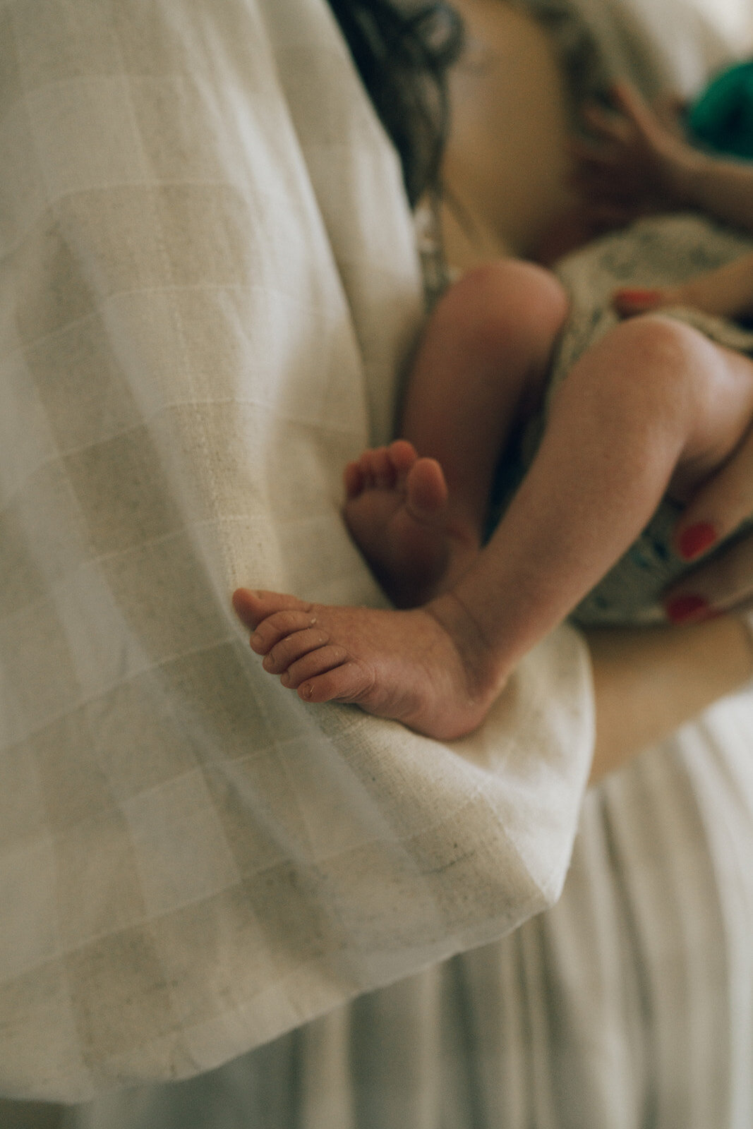 Newborn baby’s tiny feet resting in their mother’s arms during a cozy in-home newborn session