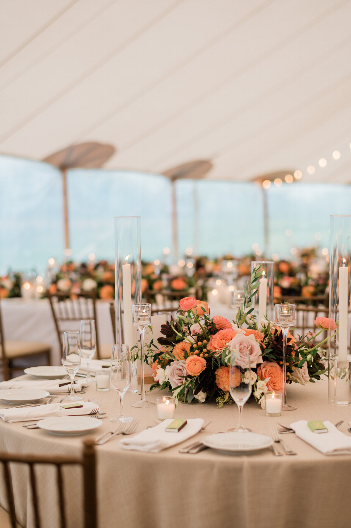 A beautifully set round table under the wedding tent at Spring Lake Golf Club, with a floral arrangement, glassware, and candles.